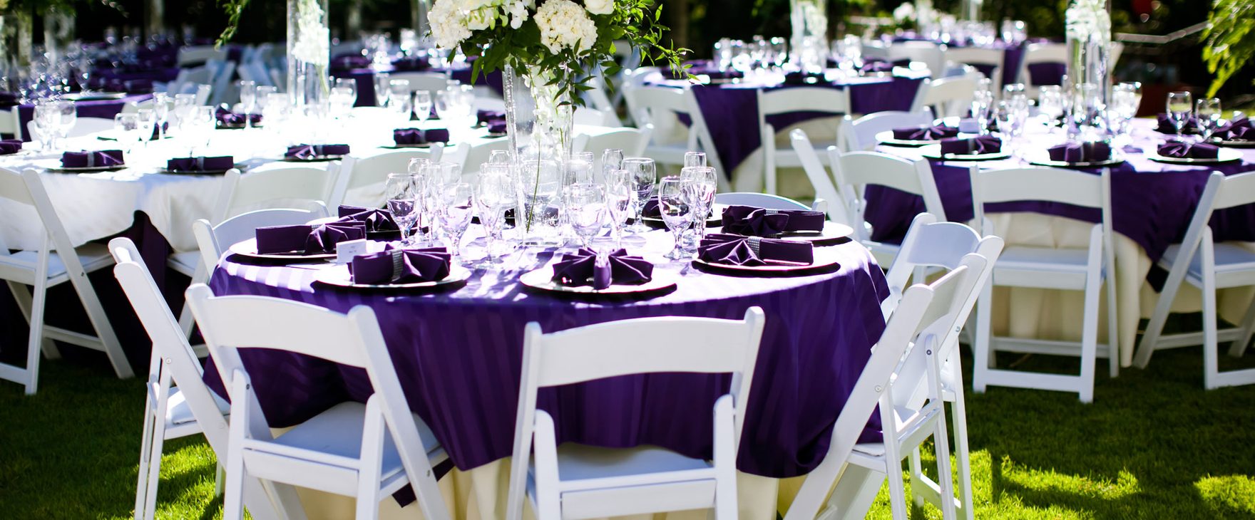 Round reception table with purple linens and folded napkins on the lawn