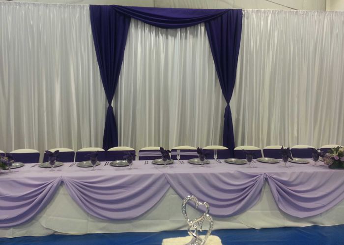 Head table with draped purple and white backdrop